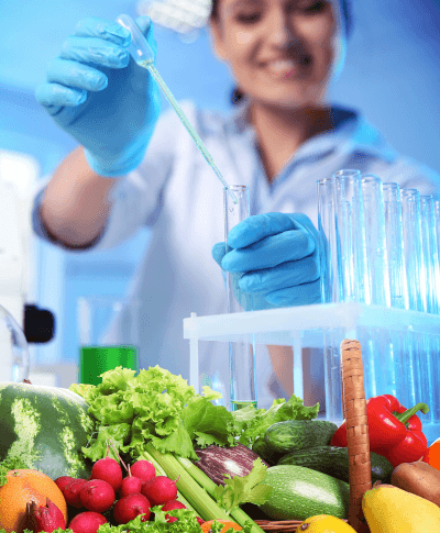 A woman tests food product ingredients using test tubes with a selection of vegetables on the lab bench