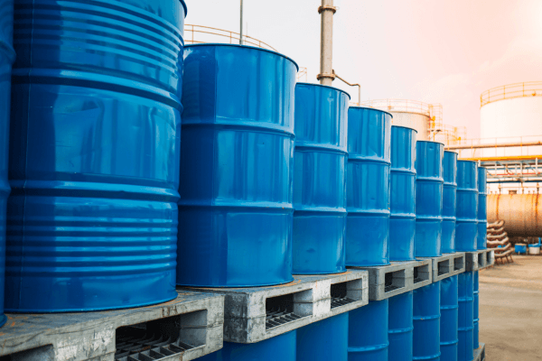 A row of large blue metal drums stacked on concrete pallets in an industrial outdoor setting at sunset.